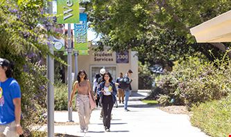 Two women walking together down MiraCosta College on a sunny day with other students around.