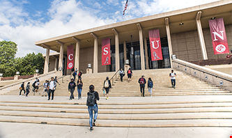 Students climbing the stairs to enter a building with 4 banners hanging between pillars to display C.S.U.N.